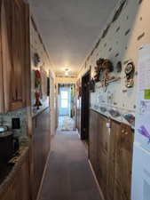 Kitchen featuring dark colored carpet, freestanding refrigerator, brown cabinets, dark stone counters, and wallpapered walls