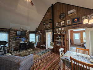 Living area with high vaulted ceiling, wooden walls, a wood stove, and a ceiling fan
