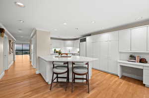 Kitchen with white cabinets, a peninsula, a breakfast bar area, light wood-style flooring, and recessed lighting