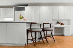 Kitchen featuring modern cabinets, white cabinetry, light countertops, light wood-style floors, and built in desk