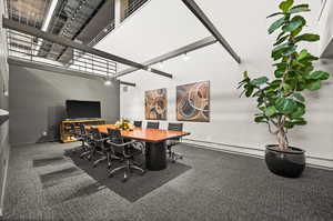 Community office featuring dark carpet, a baseboard heating unit, and a towering ceiling