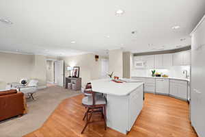 Kitchen featuring white cabinetry, open floor plan, light countertops, a breakfast bar, and light wood-style flooring