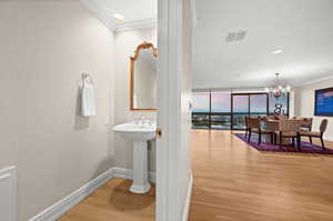 Guest half bathroom featuring expansive windows, ornamental molding, light wood-style flooring, a chandelier, and recessed lighting