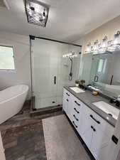 Full bathroom featuring a freestanding bath, a stall shower, double vanity, a textured ceiling, and dark wood-type flooring