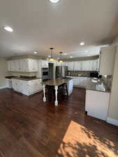 Kitchen featuring a kitchen breakfast bar, pendant lighting, dark stone countertops, white cabinets, and recessed lighting