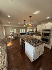 Kitchen featuring white cabinetry, dark stone counters, pendant lighting, dark wood-style flooring, and stainless steel appliances