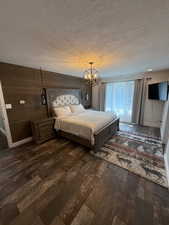 Bedroom with a textured ceiling, dark wood-type flooring, and wooden walls