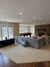 Living room with wood finished floors, a stone fireplace, a textured ceiling, pool table, and recessed lighting