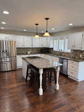 Kitchen featuring dark stone countertops, appliances with stainless steel finishes, hanging light fixtures, white cabinetry, and a kitchen island
