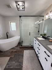 Full bathroom featuring a textured ceiling, double vanity, a freestanding tub, a stall shower, and tile walls
