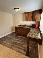 Kitchen with a textured ceiling, brown cabinetry, dark wood finished floors, dark stone counters, and a peninsula