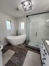 Bathroom featuring tile walls, vanity, a freestanding tub, a shower stall, and a textured ceiling