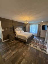 Bedroom with a textured ceiling, dark wood finished floors, a chandelier, and wooden walls