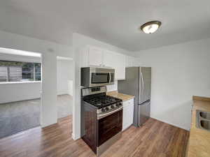Kitchen with stainless steel appliances, white cabinetry, light countertops, and dark wood finished floors