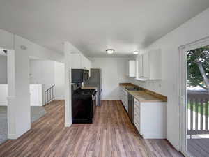 Kitchen featuring appliances with stainless steel finishes, white cabinets, dark wood-type flooring, and light countertops