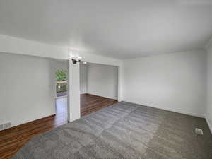 Unfurnished room featuring a chandelier, dark colored carpet, and dark wood finished floors