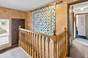 Hallway featuring an upstairs landing, carpet floors, and a textured wall