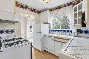 Kitchen with decorative backsplash, white cabinetry, white appliances, light wood finished floors, and under cabinet range hood