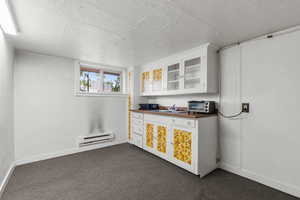 Bar area featuring white cabinets, a textured ceiling, a baseboard radiator, dark colored carpet, and glass insert cabinets