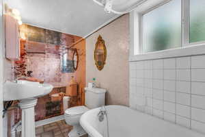 Bathroom featuring tile walls, a freestanding bath, and a textured ceiling