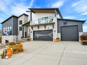 Modern home featuring stone siding, board and batten siding, driveway, and a balcony