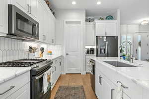 Kitchen featuring white cabinets, appliances with stainless steel finishes, light stone counters, light wood finished floors, and recessed lighting