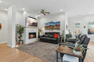 Living room with light wood-style floors, recessed lighting, a stone fireplace, and a ceiling fan