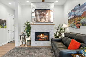 Living area with a stone fireplace, wood finished floors, and recessed lighting