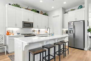 Kitchen with appliances with stainless steel finishes, light wood-type flooring, backsplash, white cabinets, and recessed lighting