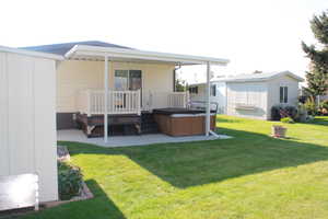 Back of property with a hot tub, a lawn, a wooden deck, and a patio area