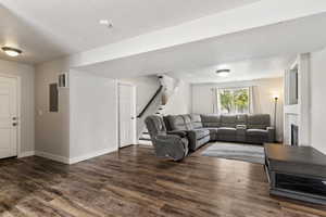 Living room with stairway, dark wood-style flooring, electric panel, and a glass covered fireplace