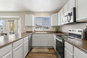 Kitchen featuring stainless steel appliances, white cabinetry, dark countertops, dark wood finished floors, and recessed lighting