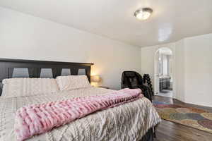 Bedroom featuring dark wood-style flooring, arched walkways, and ensuite bath