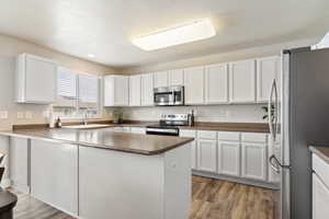 Kitchen featuring white cabinets, stainless steel appliances, dark countertops, light wood-type flooring, and a peninsula