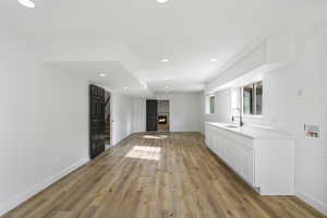 Bar area with a lit fireplace, recessed lighting, light wood finished floors, and white cabinets