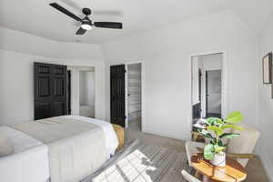 Carpeted bedroom featuring a walk in closet, vaulted ceiling, ceiling fan, and ensuite bath