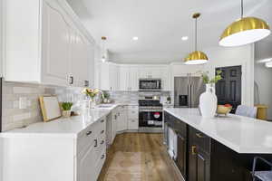 Kitchen featuring appliances with stainless steel finishes, hanging light fixtures, white cabinetry, decorative backsplash, and recessed lighting