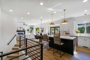 Kitchen featuring white cabinets, a tiled fireplace, hanging light fixtures, light wood-type flooring, and decorative backsplash