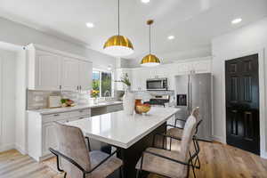 Kitchen featuring stainless steel appliances, hanging light fixtures, white cabinetry, a breakfast bar, and light wood-style flooring