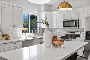 Kitchen with white cabinetry, light stone counters, appliances with stainless steel finishes, pendant lighting, and backsplash