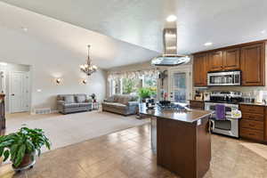 Kitchen featuring stainless steel appliances, dark stone counters, island exhaust hood, vaulted ceiling, and a kitchen island