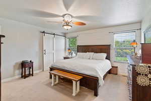 Bedroom featuring light carpet, a barn door, multiple windows, a ceiling fan, and a textured ceiling