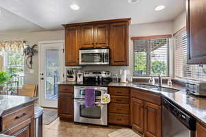 Kitchen with appliances with stainless steel finishes, dark stone countertops, light tile patterned floors, recessed lighting, and brown cabinets