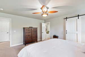 Bedroom featuring a barn door, light colored carpet, and a ceiling fan