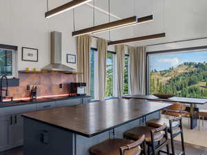 Kitchen featuring wall chimney range hood, a breakfast bar, a kitchen island, tasteful backsplash, and white cabinets