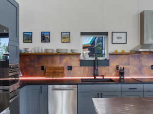 Kitchen with wall chimney exhaust hood, open shelves, appliances with stainless steel finishes, and tasteful backsplash