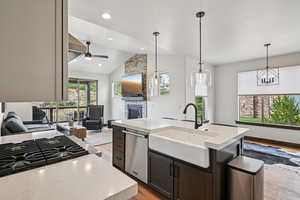 Kitchen featuring light wood finished floors, open floor plan, a fireplace, decorative light fixtures, and a kitchen island with sink