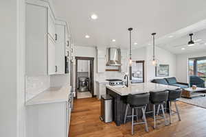 Kitchen featuring open floor plan, light wood-style flooring, an island with sink, light stone countertops, and pendant lighting