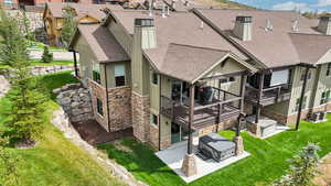 Back of house with stone siding, a chimney, roof with shingles, and a wooden deck