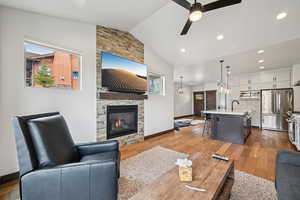 Living room with vaulted ceiling, light wood-type flooring, a ceiling fan, a stone fireplace, and recessed lighting